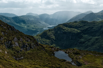 A small lake sits on the hillside, overlooking the beautiful Gap of Dunloe valley. Rolling green mountains stretch into the distance in County Kerry, Ireland.