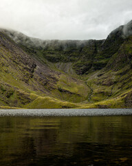 Clouds caress the peaks of the dramatic mountains, their reflections dancing on the still water below.