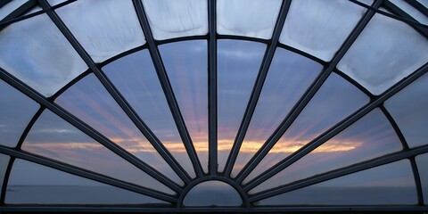 A stunning architectural design features a circular metal and glass roof, reminiscent of an open parasol against the blue sky, atop a modern building