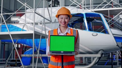 Asian Female Engineer With Safety Helmet Smiling And Showing Green Screen Laptop To The Camera With Inspecting Helicopter Assembly