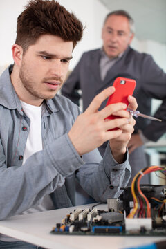 angry teacher behind electrician apprentice looking at his smartphone