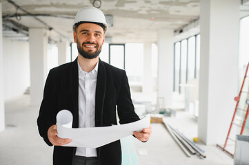 Smiling architect holding blueprints in building under construction