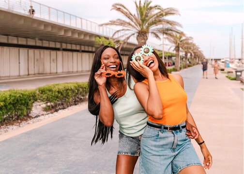 Two cheerful female friends enjoying a summer day wearing funny sunflower glasses laughing outdoors