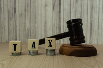 Wooden blocks spelling the word 'TAX' placed on coins beside a judicial gavel on a wooden surface. Wooden Blocks and Gavel Representing Legal Tax Implications and Justice Concept