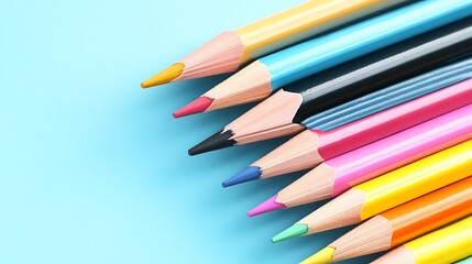 Fototapeta premium A collection of colorful pencils arranged neatly in a fan shape, placed on a pastel blue solid background, showcasing sharp tips and vibrant hues.