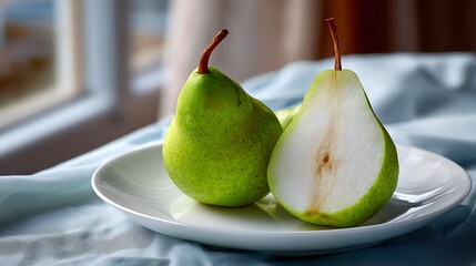 Whole and Halved Green Pear on a White Plate