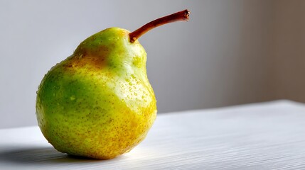 A single green-yellow pear with a brown stem resting on a light surface