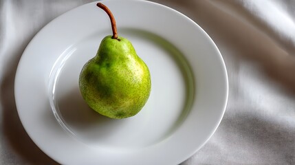 A single green pear placed on a white plate against a soft background