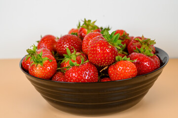A black bowl filled with bright red strawberries, highlighting their juicy appearance and green leafy tops. The vibrant colors create an inviting and refreshing look