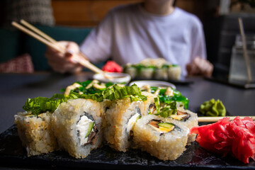 Closeup hand holding bamboo chopsticks with nigiri shrimp while soaking it in soy sauce. Detail of...