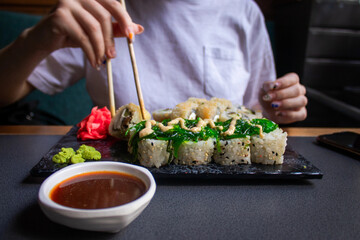 Closeup hand holding bamboo chopsticks with nigiri shrimp while soaking it in soy sauce. Detail of...