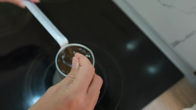 Stirring coffee in a copper cezve, close-up of female hand make coffee on induction ceramic stove in stainless steel metal Turk.