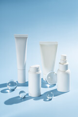 Mockup of white plastic bottles and tubes with face serum or cream, or toner on blue background with glass balls. The concept of beauty cosmetics, natural products for moisturizing and restoring skin.