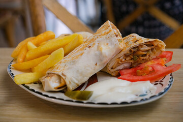 Delicious serving of chicken shawarma wrap with crispy French fries, fresh tomato slices, pickles, and a side of white garlic sauce.