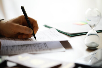 Hand Signing Important Documents with Pen and Hourglass on Desk