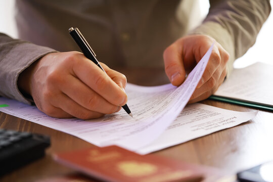Close-up of Person Filling Out Form with Passport on Desk - Administrative Work and Documentation