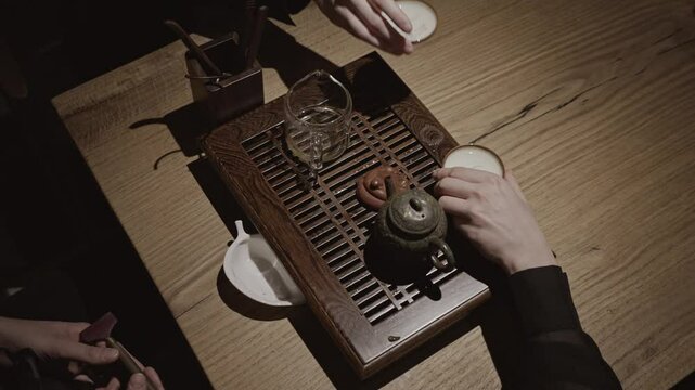 A tea master gracefully pours brewed tea from a glass teapot into two ceramic bowls during a traditional tea ceremony.