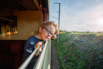 Smiling boy leans out carriage window against fields backdrop