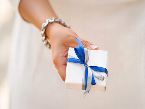AI-Generated Close-up of Woman’s Hand Giving Gift Box with Blue and Silver Ribbon