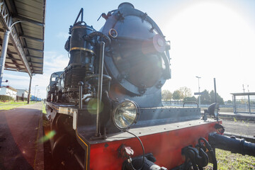 Steam locomotive stands at platform in sunlight under blue sky