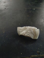 Crumpled and dirty light colored used tissues are placed on a dark and textured surface. The...
