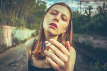 Portrait of a stylish woman holding a cigarette, standing outdoors in soft natural light....