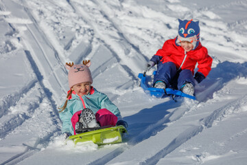 Children sledding down a hill, enjoying sunny winter adventure