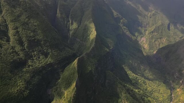 A breathtaking drone shot captures steep, deeply creased mountain slopes covered in dense dark green vegetation.