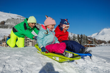 Joyful kids slide down a snowy slope in bright winter jackets