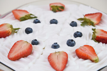 Tres Leches Cake in a clear glass baking dish topped with fluffy whipped cream garnished with vibrant fresh strawberry and blueberries closeup side view of moist dessert