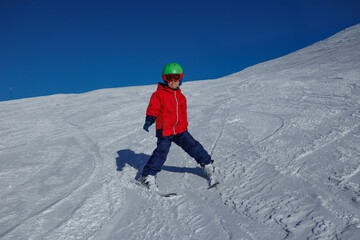 Young skier in red jacket practices wedge turns on a snowy slope