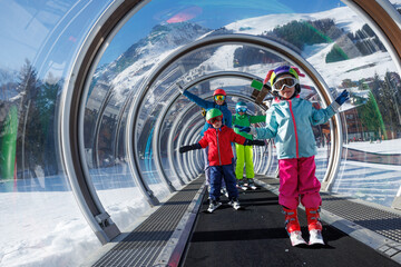 Skiers kids and adults ascending through a glass-enclosed lift