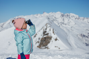 Kid in winter wear enjoys snowy mountain view through binocular