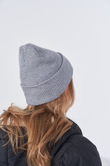 Woman with long wavy light brown hair wears a gray ribbed knit beanie and a black puffer jacket,...
