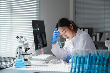 Asian scientist woman wearing lab coat and gloves having a headache in a laboratory with microscope...
