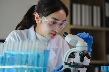 Scientist wearing lab coat and gloves using microscope analyzing sample in laboratory with test...