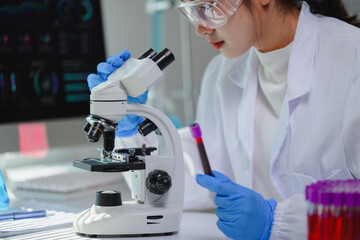 Scientist wearing lab coat and gloves using microscope and holding blood sample in laboratory