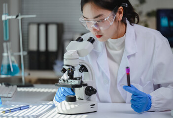 Scientist wearing lab coat and protective glasses analyzing blood sample and using microscope in...