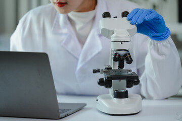 Scientist adjusting microscope while working with laptop in laboratory