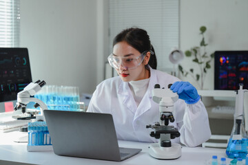 Scientist using microscope and laptop, performing scientific research in modern laboratory