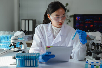 Young scientist wearing lab coat and gloves analyzing test tube with blue liquid while holding a...