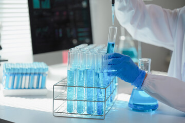 Scientist wearing lab coat and gloves adding blue liquid to test tube using pipette, working with...