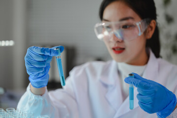 Scientist wearing lab coat and gloves comparing two test tubes with blue liquid during experiment...