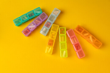 Medicine and health concept. Multicolored pill organizers with different pills, supplements, on yellow background with top view. Organizer for multivitamins, capsules, health supplements.