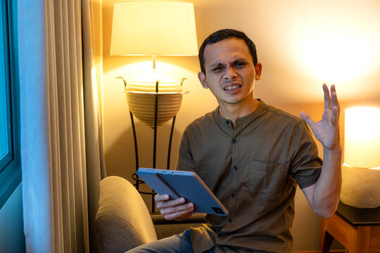 Annoyed man reacting to problem while using tablet in cozy indoor setting