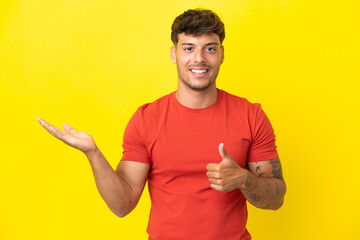 Young caucasian handsome man isolated on yellow background holding copyspace imaginary on the palm...