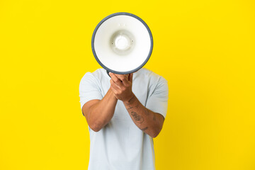 Young caucasian handsome man isolated on yellow background shouting through a megaphone to announce...
