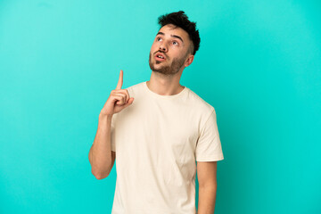 Young caucasian man isolated on blue background thinking an idea pointing the finger up