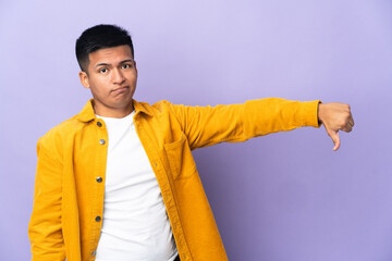 Young Ecuadorian man isolated on purple background showing thumb down with negative expression