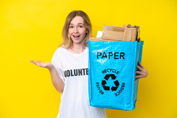 Blonde English young girl holding a recycling bag full of paper to recycle isolated on yellow...